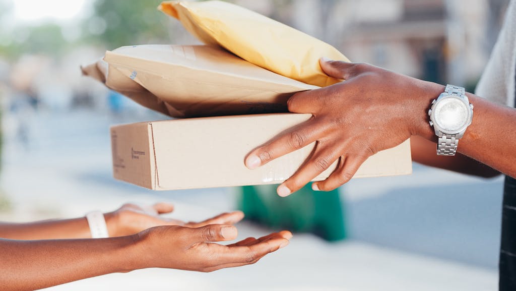 Hands exchanging packages — representing dispatch and delivery.