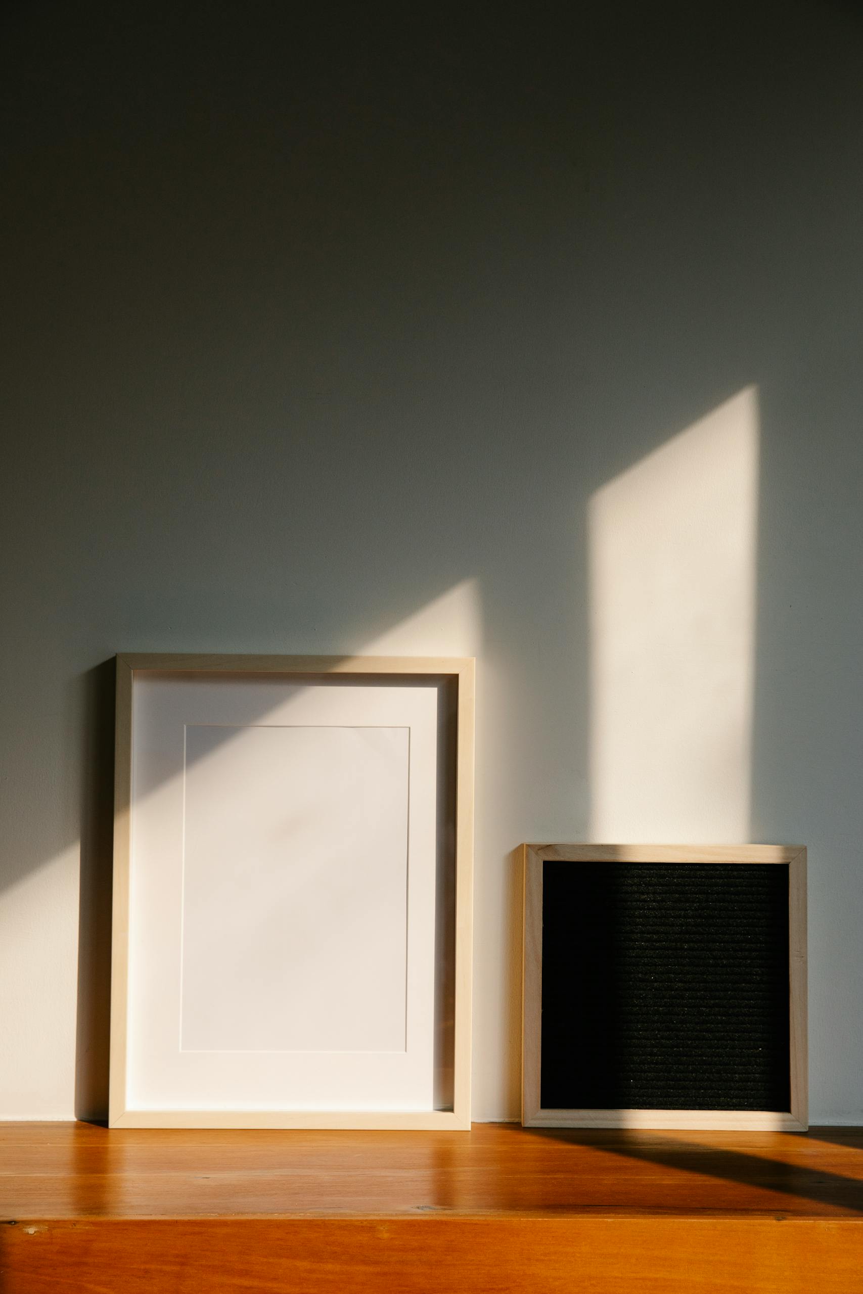 Minimalist wooden frames casting shadows on a wooden surface in sunlight.