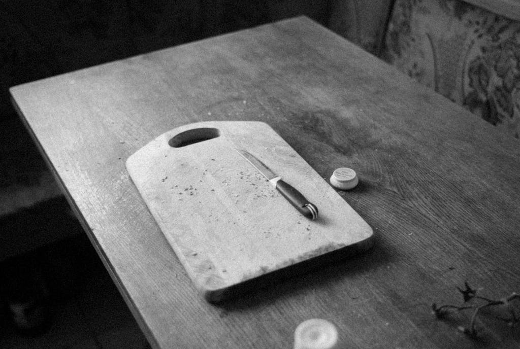 Monochrome image of a wooden chopping board with a knife in a rustic kitchen setting.