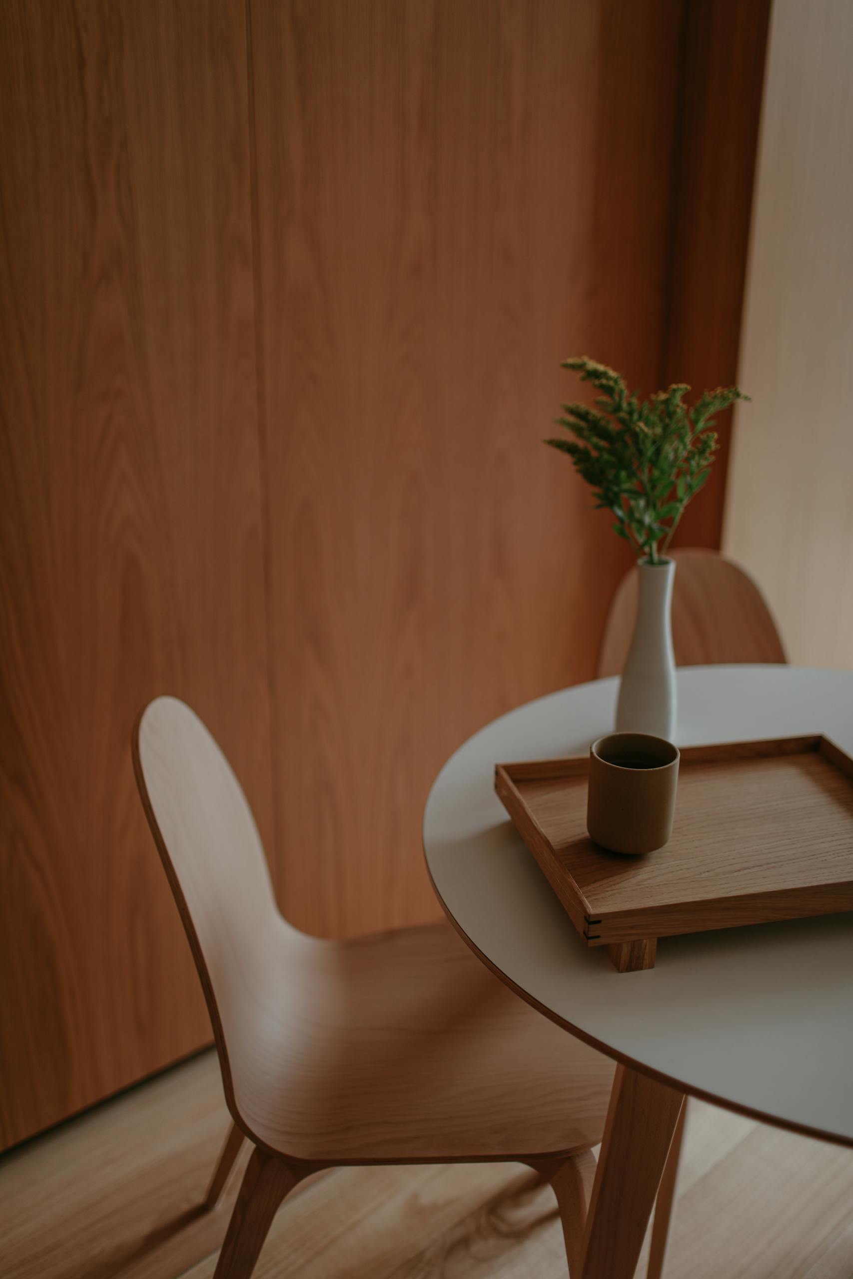Stylish minimalist dining setting with wooden features, a tray, and a vase on a round table.